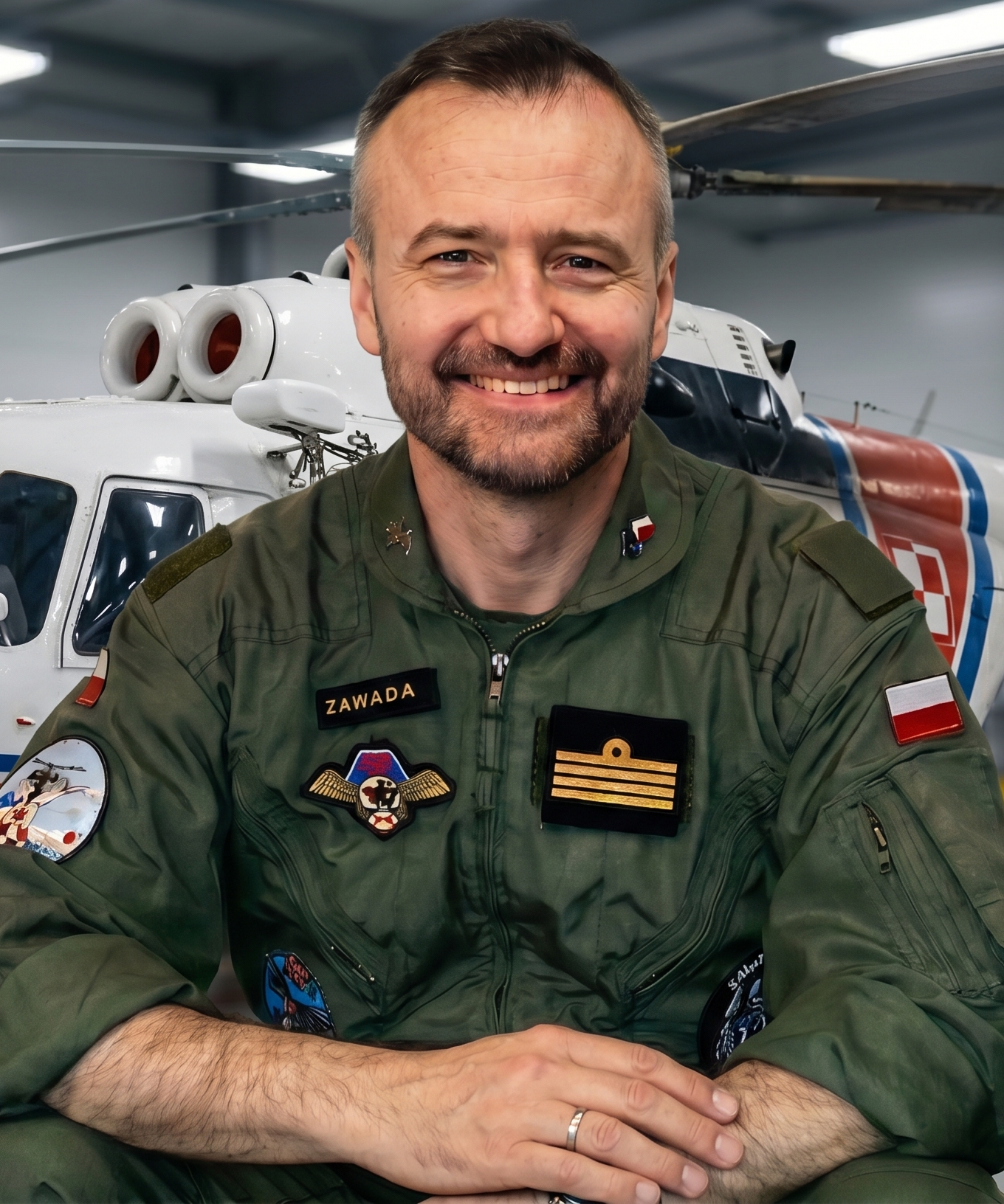 Kpt. rez. pil. Robert Zawada w mundurze lotniczym, w hangarze przed śmigłowcem Marynarki Wojennej RP